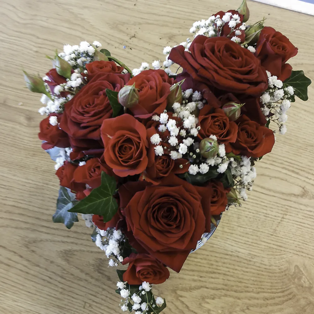 Blumengesteck in Herzform mit roten Rosen und kleinen weißen Blumen